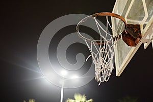 Basketball hoop with broken net - detail - night scene of playground exterior with shining lamp