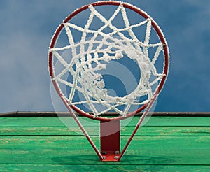 A basketball Hoop with a net in the frost on blue sky background close up shot from below