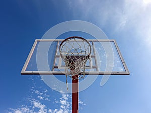 Basketball hoop with net on an outdoor court with sky background from below