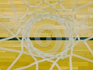 Basketball hoop in the sports hall. Look down through white string net, hardwood board