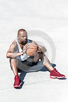 Basketball player with ball in hands sitting on court