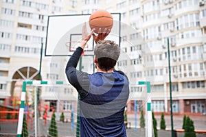 A basketball player at an outdoor stadium trains, throwing a ball into the ring, lifting his hands up.