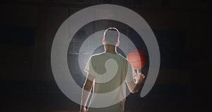 Basketball player silhouette plays with a ball twists on a finger a shadow darkness back view