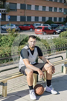 Basketball player sitting next to his basketball ball on an urban court, waiting to go out to play