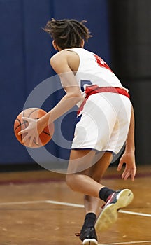 Basketball player in white uniform dribbling the ball down the court