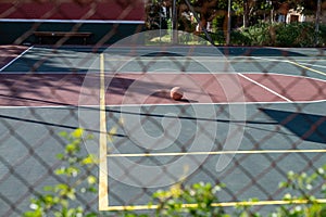 Basketball seen on empty court seen through chain link fence