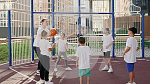 Basketball training session with coach. Teacher playing with children a game with ball in the school yard. Sport and