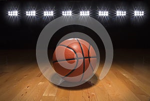 Basketball on wood floor beneath bright lights