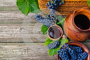 Baskets and bowl with grapes beside Jar and cup with wine stand on on rustic wood. Wine making background.