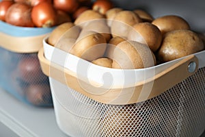 Baskets with potatoes and onions on shelf. Orderly storage