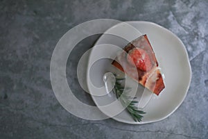 Basque burnt cheesecake with fresh strawberries on white plate cement floor background.