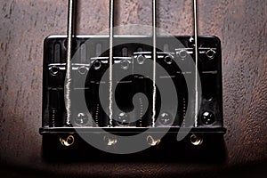 Bass electric guitar with four strings closeup. Detail of popular rock musical instrument. Vintage photo of metal bridge of brown
