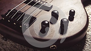 Bass electric guitar with four strings closeup. Detail of popular rock musical instrument. Vintage style photo of control knobs of