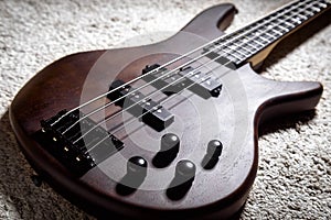 Bass guitar with four strings. Popular rock musical instrument. Close view of brown electric bass on carpet