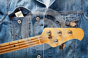 Bass guitar headstock and one dollar bills in the pocket of  denim jeans jacket