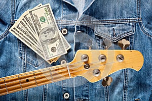 Bass guitar headstock and one hundred dollar bills on denim jeans jacket