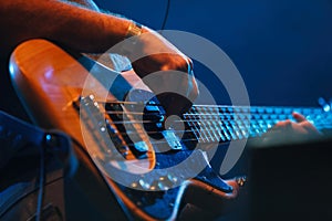 Bass guitar player performing on concert. Close up photo of professional guitarist playing solo part on stage