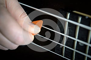Bass guitar player with pick in his hand closeup, lesson and practice theme. Playing on bass electric guitar, live music and skill