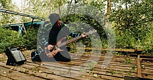 The bass guitarist plays on his knees on the old wooden pier.