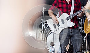 Bass guitarist in a rock or heavy metal band in a red and black plaid flannel shirt playing bass guitar on stage at a festival