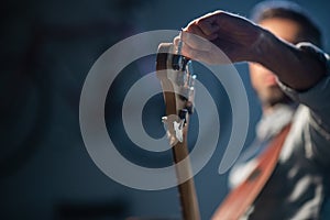 The bassist adjusts the electric bass guitar, in the foreground of the pegs and fretboard, close-up.