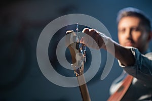 The bassist adjusts the electric bass guitar, in the foreground of the pegs and fretboard, close-up.