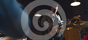 Bassist with his guitar. Wide indoor shot of caucasian mid adult male musician in grey blazer playing on his guitar.