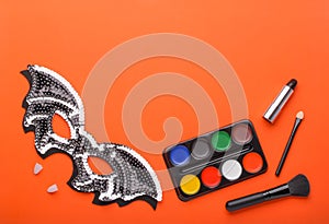 Bat-mask and vampire fangs and cosmetics on an orange background.