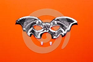 Bat-mask and vampire fangs on an orange background.