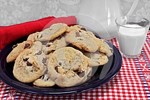 A batch of chocolate chip walnut cookies on a plate with a glass