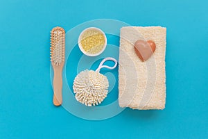 Bath accessories: towel, salt, brush, wisp, pumice and soap on blue background. Spa cosmetic or hygiene concept. Copy space. Flat