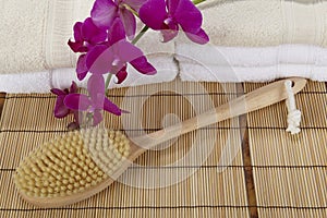 Bath brush on a bamboo mat, towels and a orchid