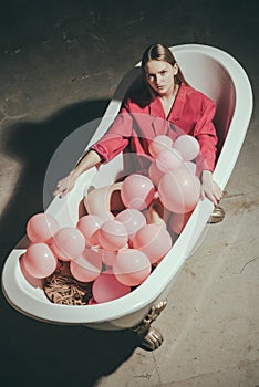 Bath filled with pink balloons and woman relax in bathroom.