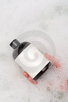 Bath foam bottle mockup for packaging. In a woman's hand. Foam in the background. Place for text and logo