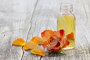 Bath oil and orange rose on wooden background