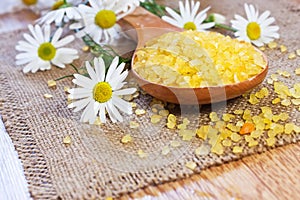 Bath salt on wooden spoon with chamomile on mat