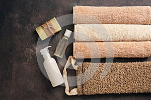 Bath and spa accessories, terry towel, soap, loofah washcloth and oil on a dark rustic background. Flat lay, top view