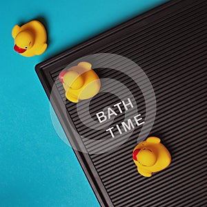 Bath time -  text on black letter board with yellow rubber ducks on blue background. Top view, flat lay. Bath concept