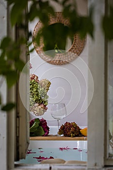 Bath tub with flower petals, grapefruit slices, bunch of grapes and a glass