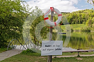 Bathing establishment with lake, in the foreground white-red rescue ring with warning sign german text translation: swim in the