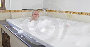 Bathing Young Woman Relaxing In Bath Full Of Foam Raising Legs, Smiling Beautiful Girl Enjoys Spa At Home