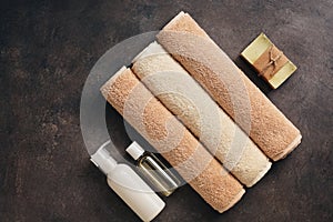 Bathroom accessories, terry towel, handmade soap, shampoo and oil on a dark brown rustic background. Top view, flat lay, copy
