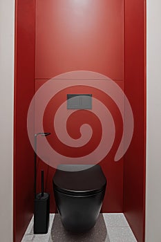 Bathroom with black toilet, red wall, wood flooring, and door