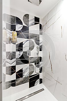 Bathroom with black white tiles, where a modern shower cabin without a pallet with chrome mixtures in modern style