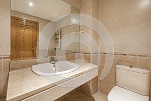 Bathroom with chunky cream marble countertop with white porcelain recessed sink below frameless mirror and cream tiled valanced