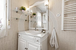 Bathroom with cream tiled walls and floors and white wooden bathroom cabinet with white porcelain sink with mirror and matching