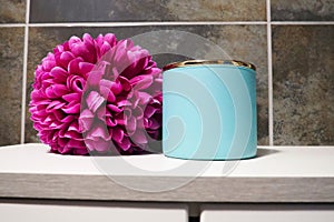 Bathroom decor elements. A blue jar of bath cream or bath salt, and a bright pink artificial double flower on a cabinet