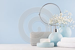 Bathroom decor for female in light soft blue color - circle mirror, silver cosmetic bag, white flowers, towel, soap and vase.