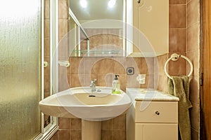 Bathroom with frameless mirror, white porcelain sink with matching pedestal, and walk-in shower with white accents and brown tiles