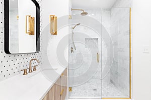 A bathroom with gold faucets and a shower lined with marble tiles.